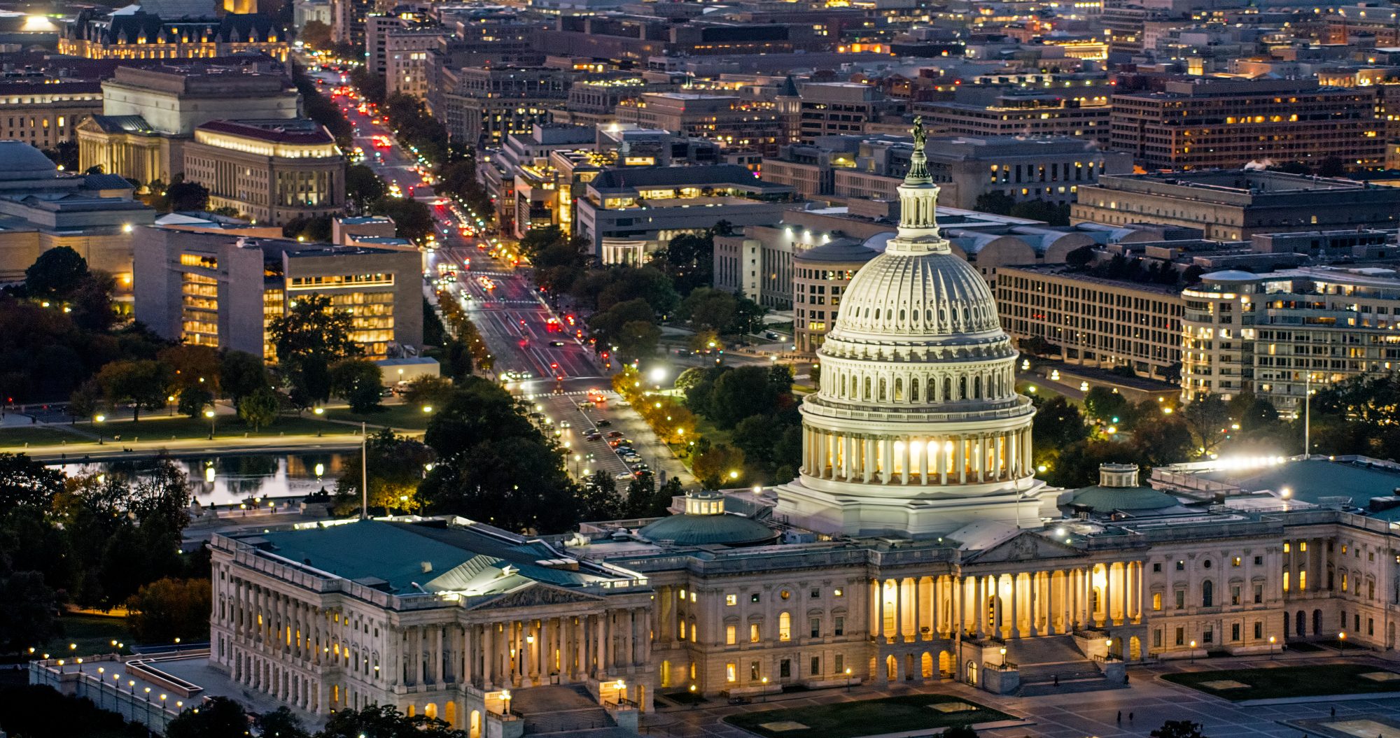 High angle helicopter shot of the Capitol Building in Washington, D.C. at twilight on a clear evening in Fall, with Pennsylvania Avenue beyond.