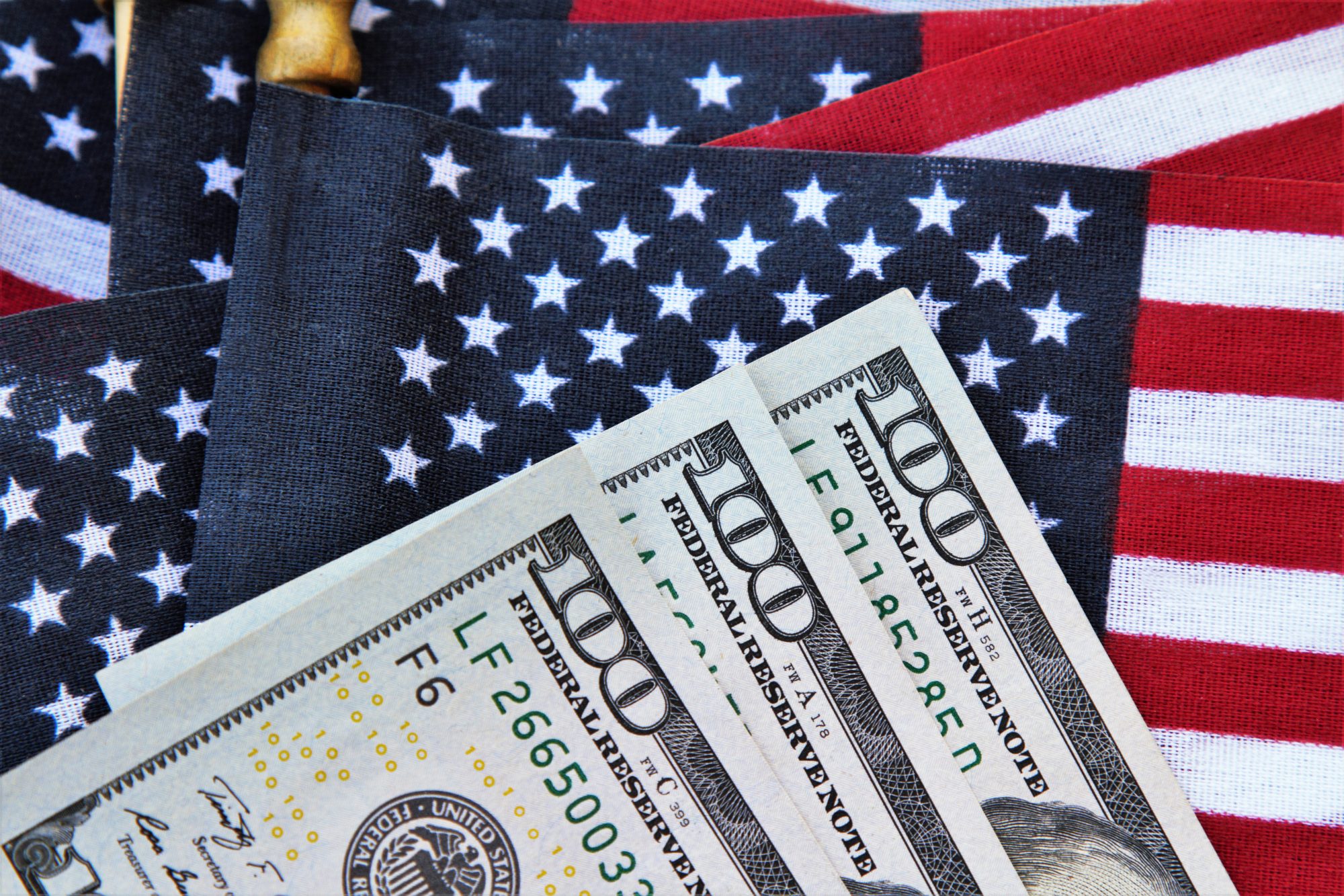 Three one hundred dollar bills partial view on top of group of American flags. Concept image for  government payments for corona virus relief, IRS refund or other financial payments.